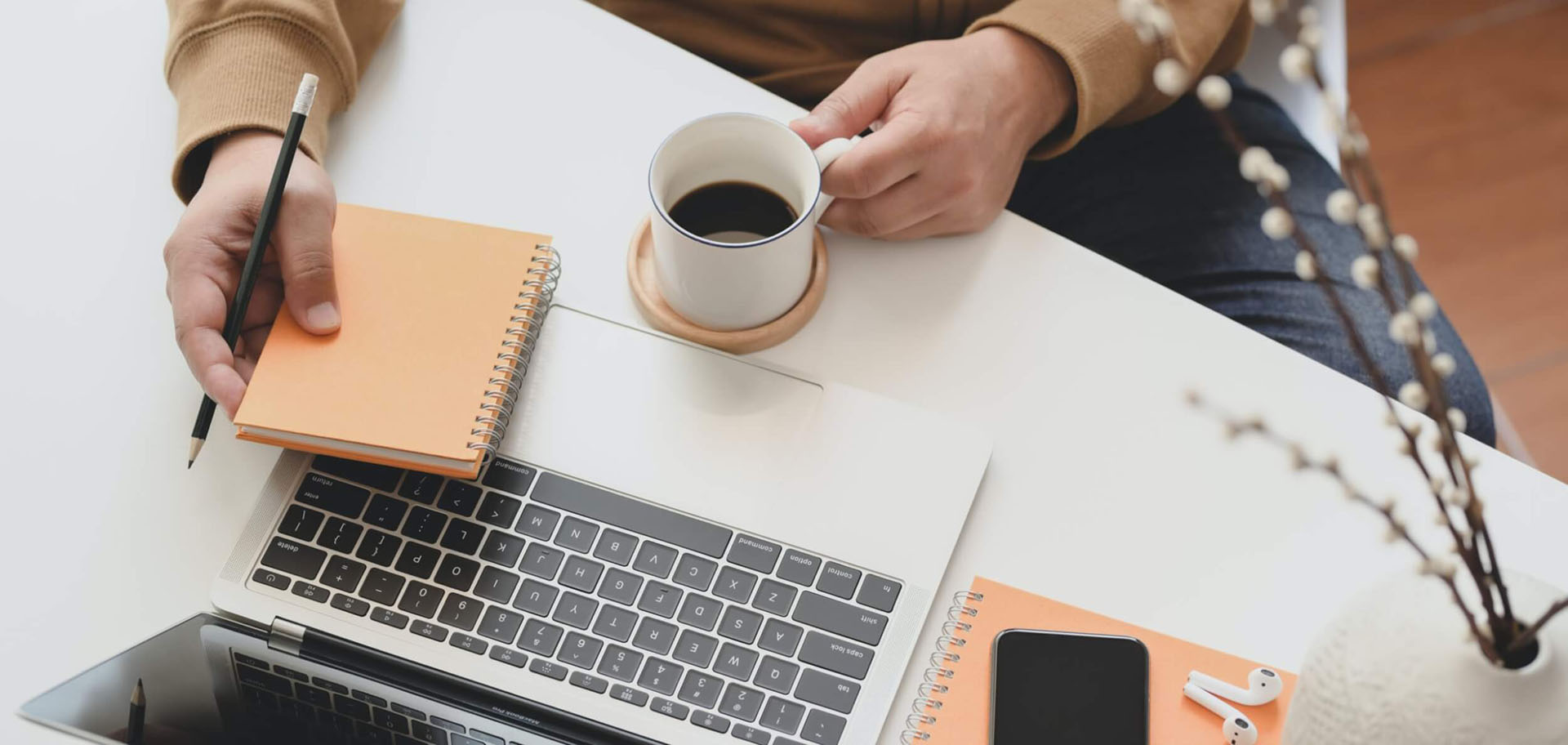 A person at a desk with a laptop, notebook, and cup of coffee