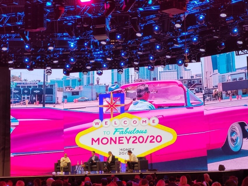 a group of people sitting on stage in front in front of a large screen showing a pink Cadillac