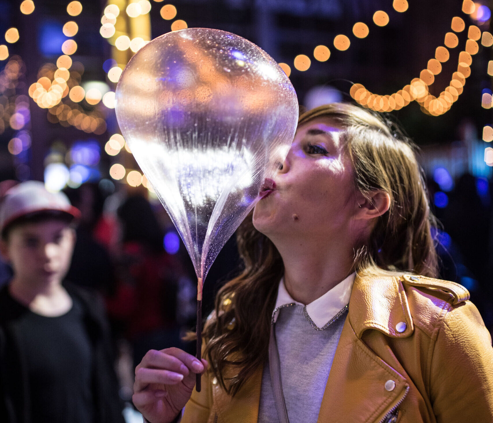 a woman wearing a yellow jacket, kissing a clear balloon