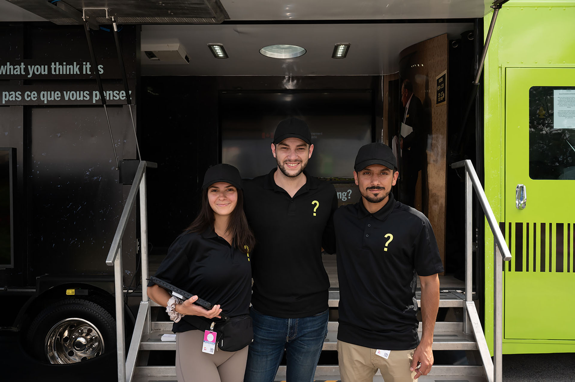Three people in black t-shirts standing in front of a black and green truck
