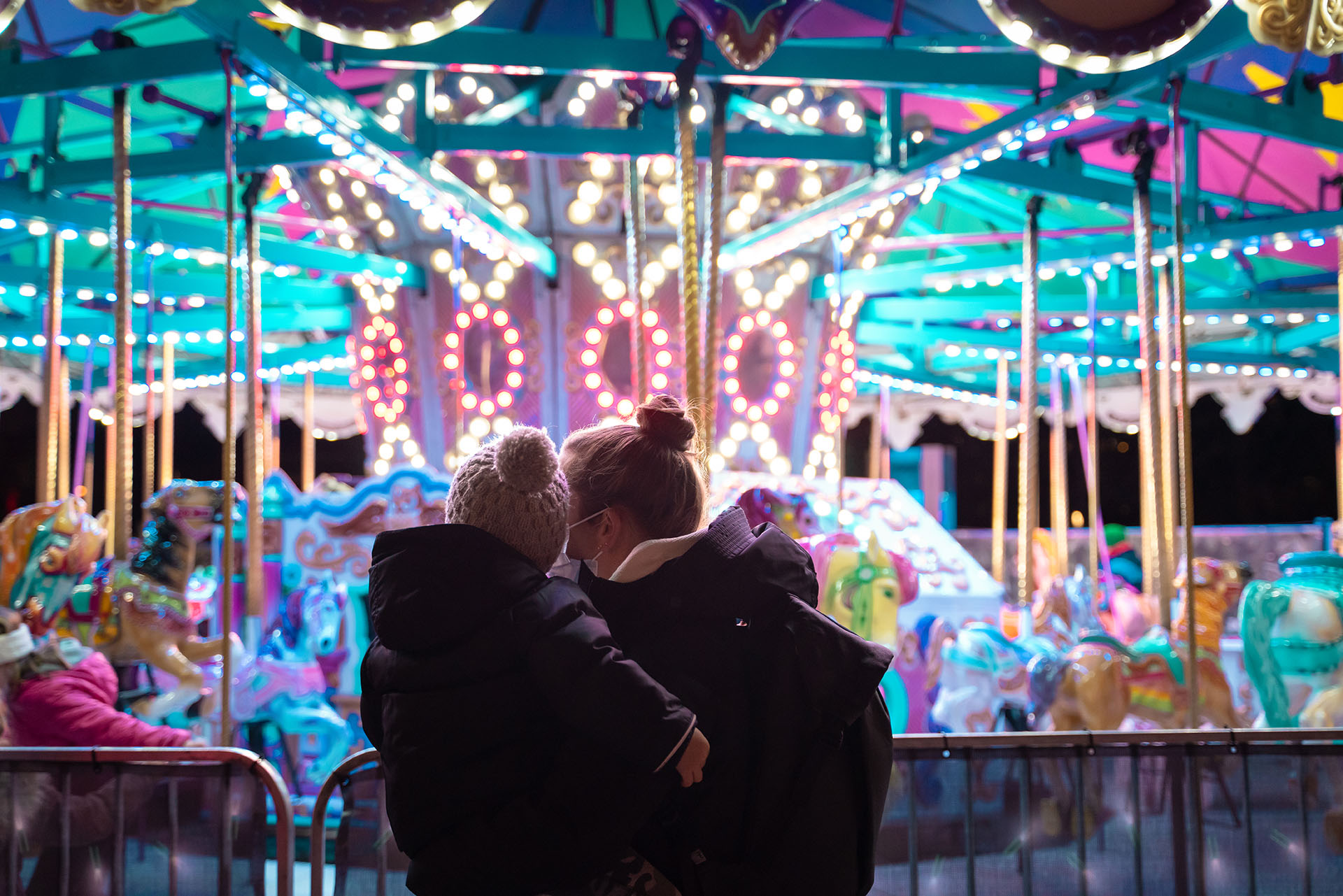 A women holding a child in front of a merry-go-round