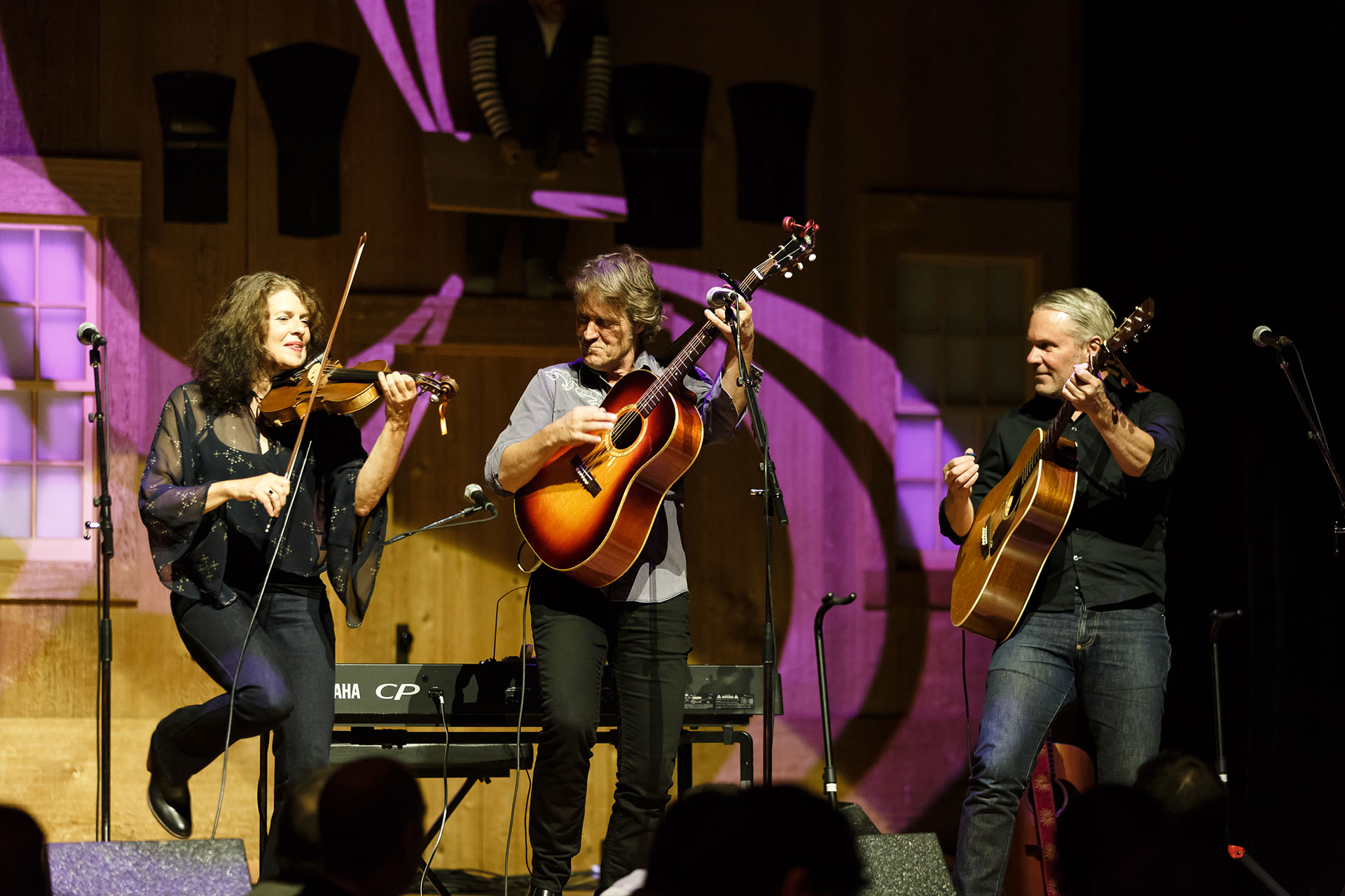 Two men with guitars and a woman with a violin performing on stage
