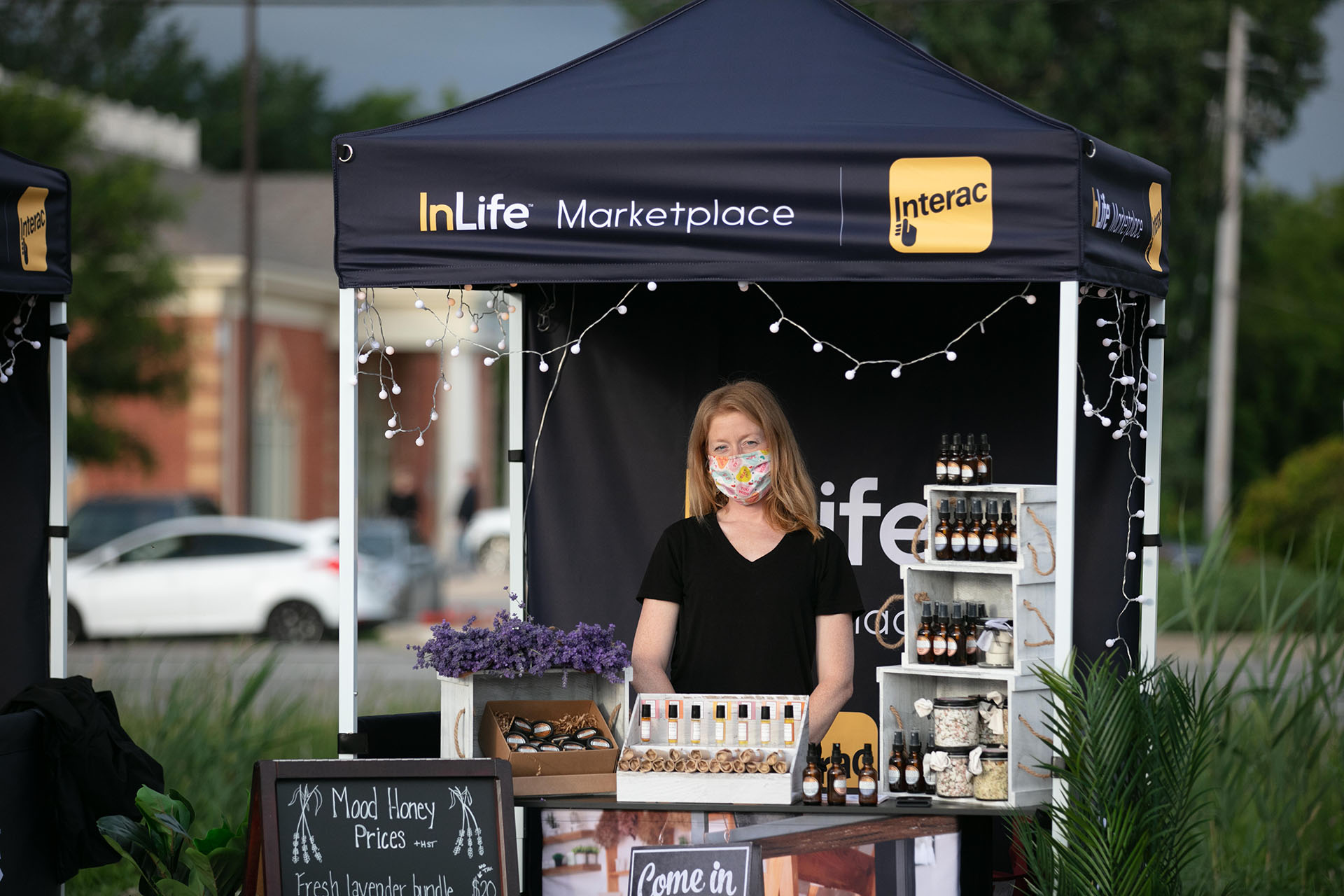 A woman wearing a mask standing at a InLife Marketplace sample stand