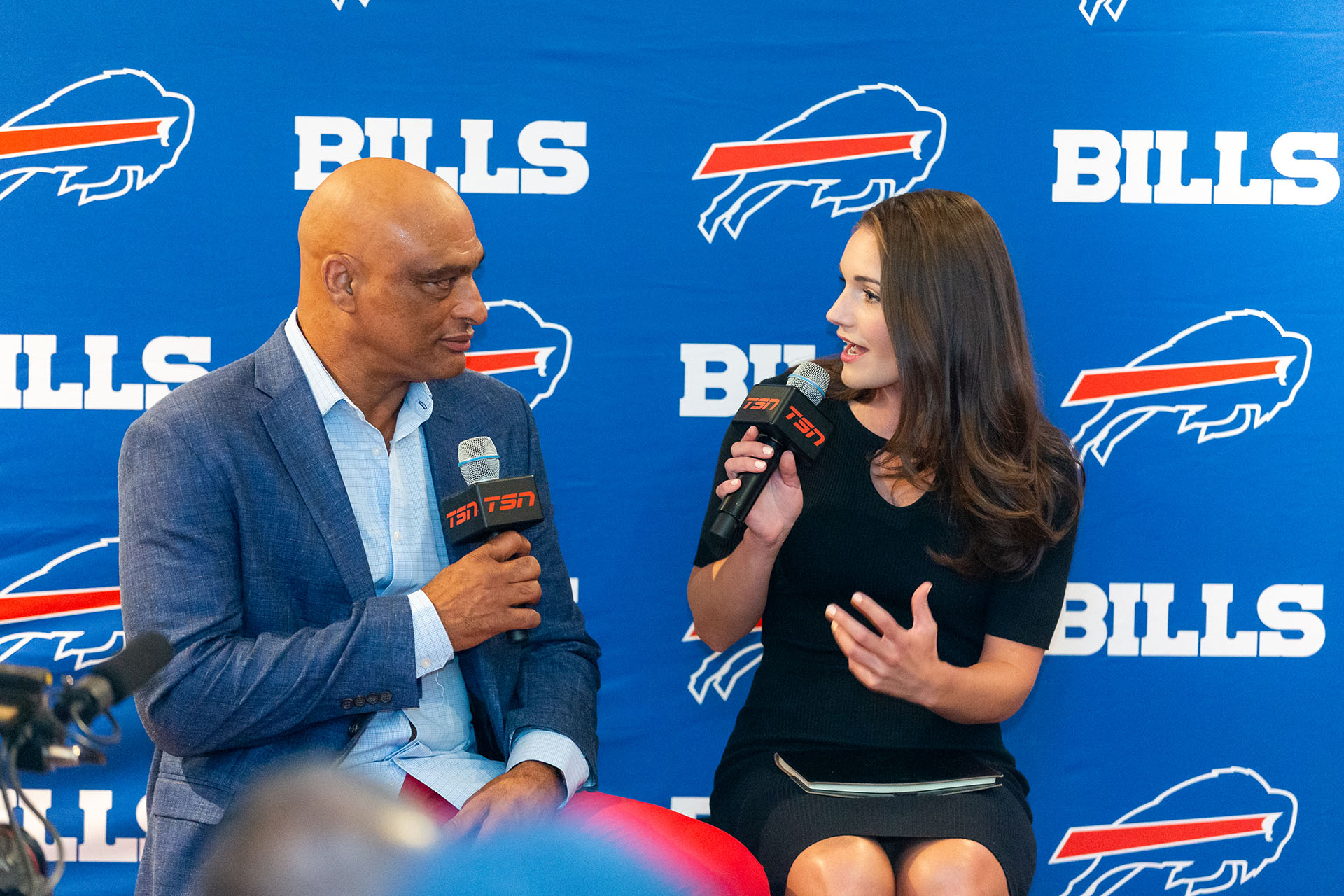 Two people speaking in front of a Buffalo Bills wall