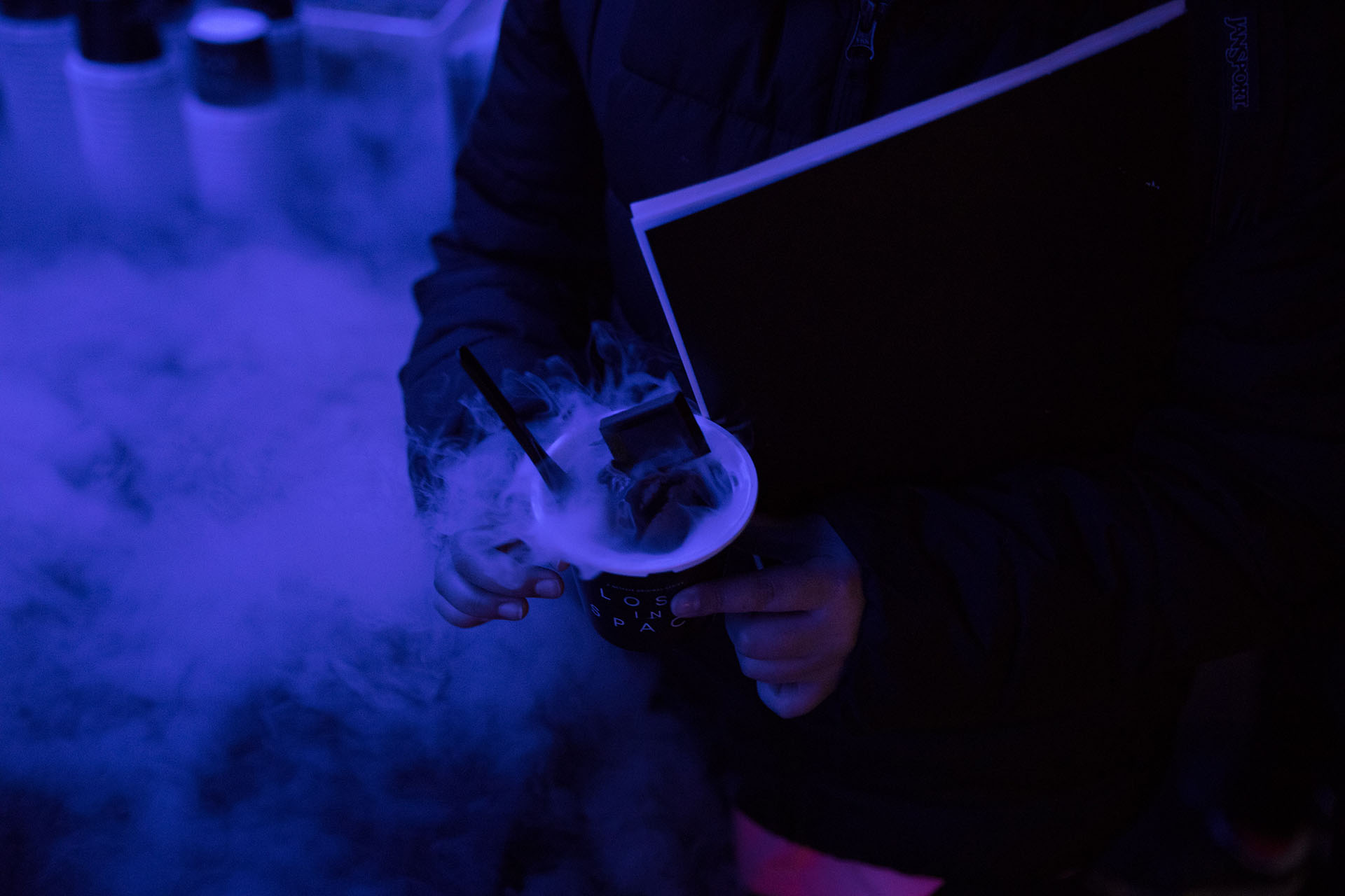 Someone standing in black fog smoke holding a beverage