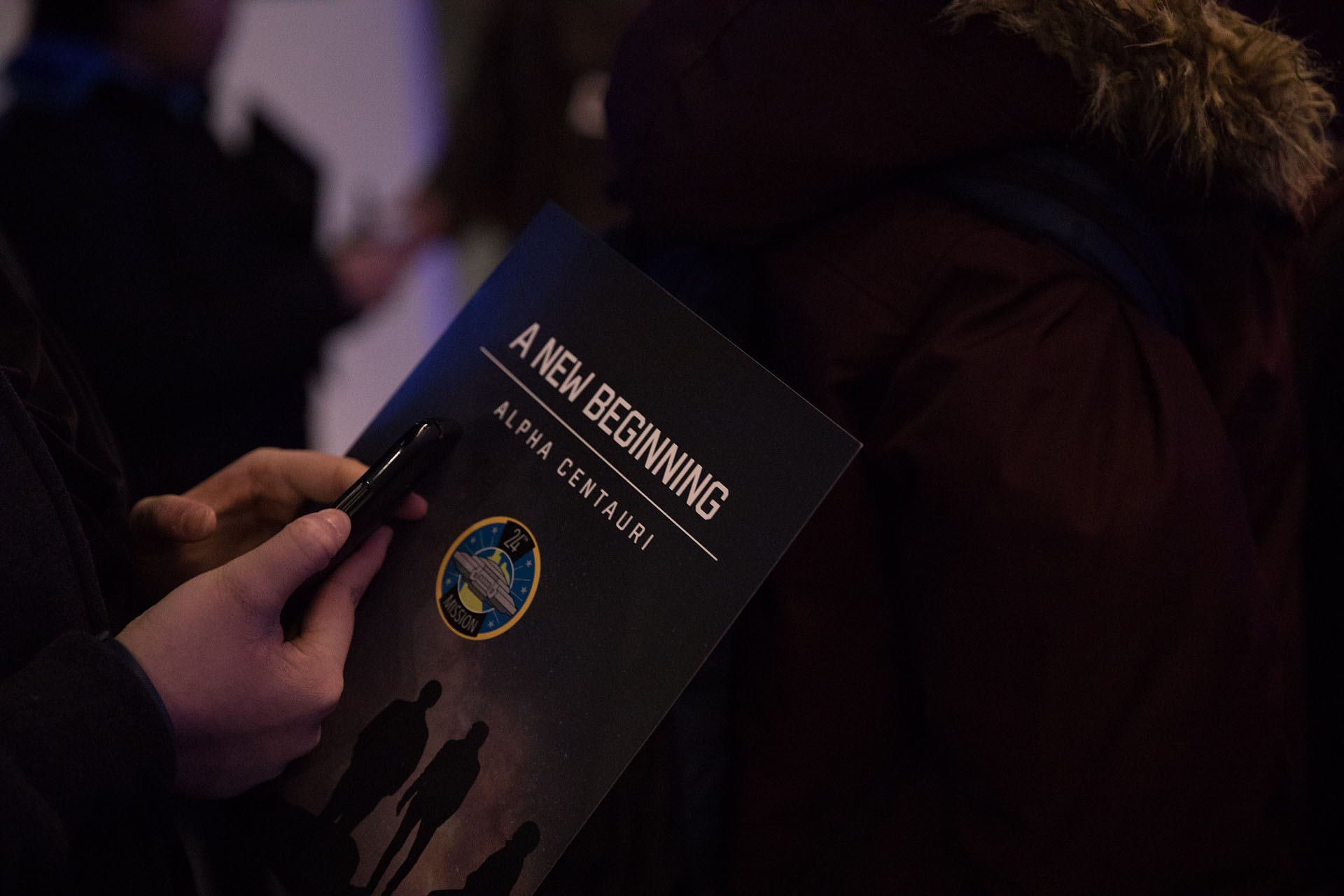 Someone is holding a phone and a paper with 'A New Beginning - Alpha Centuri on the front
