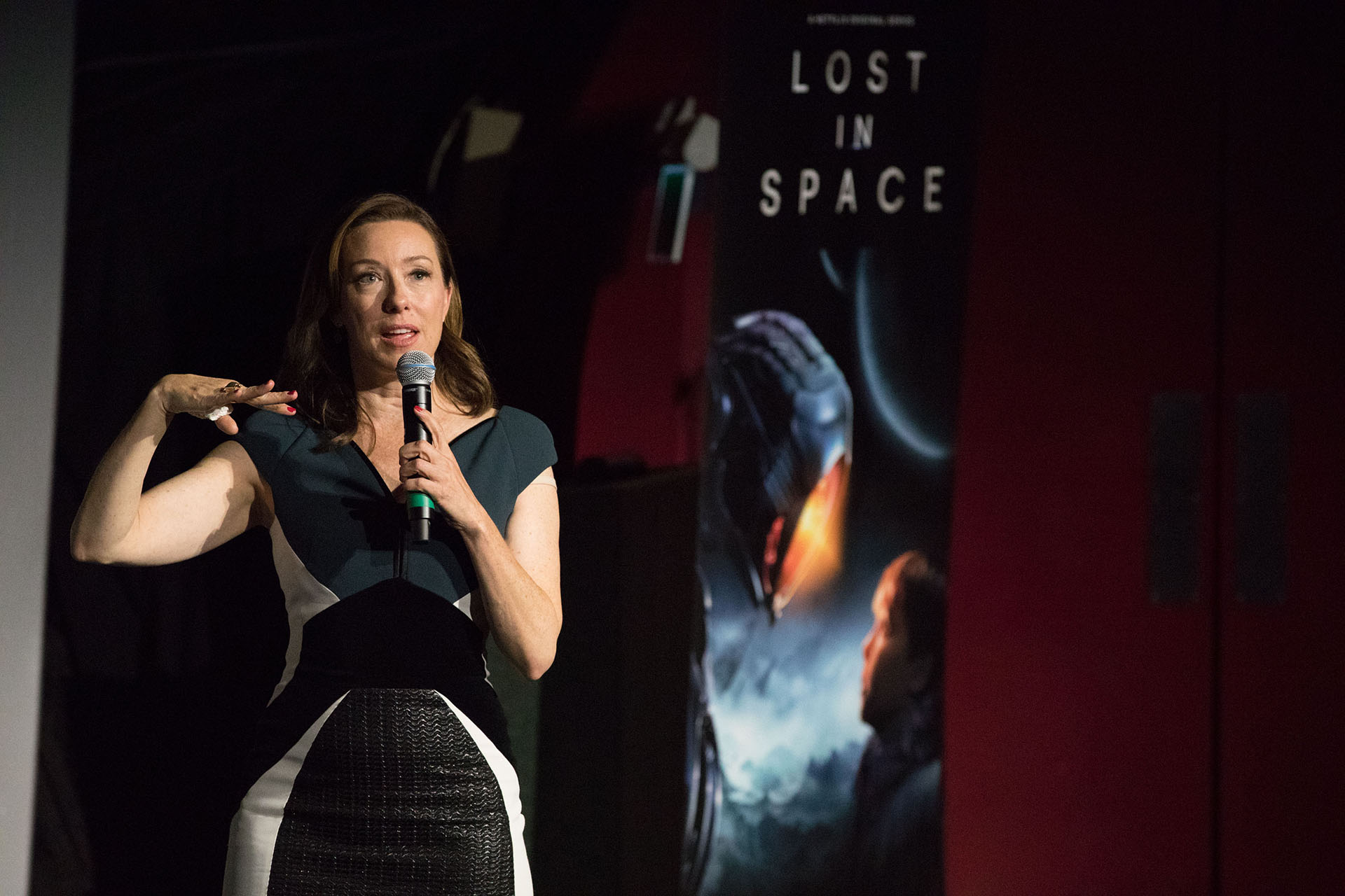 Molly Parker wearing a dress and holding a mic in front of a Lost in Space sign