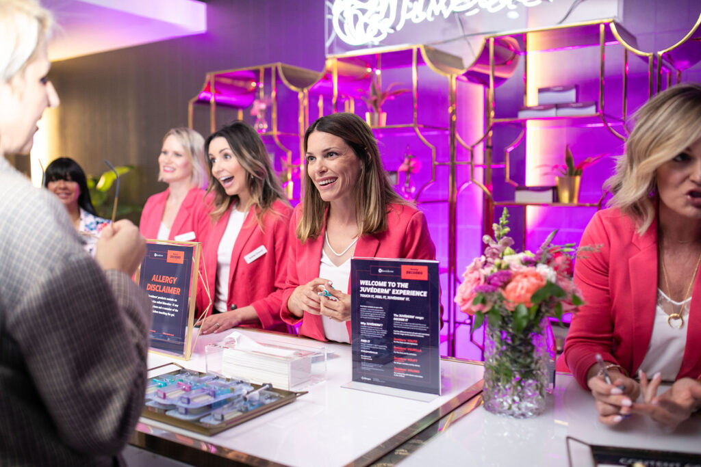A group of women wearing red blazers speaking to guests at a Juvederm display stand