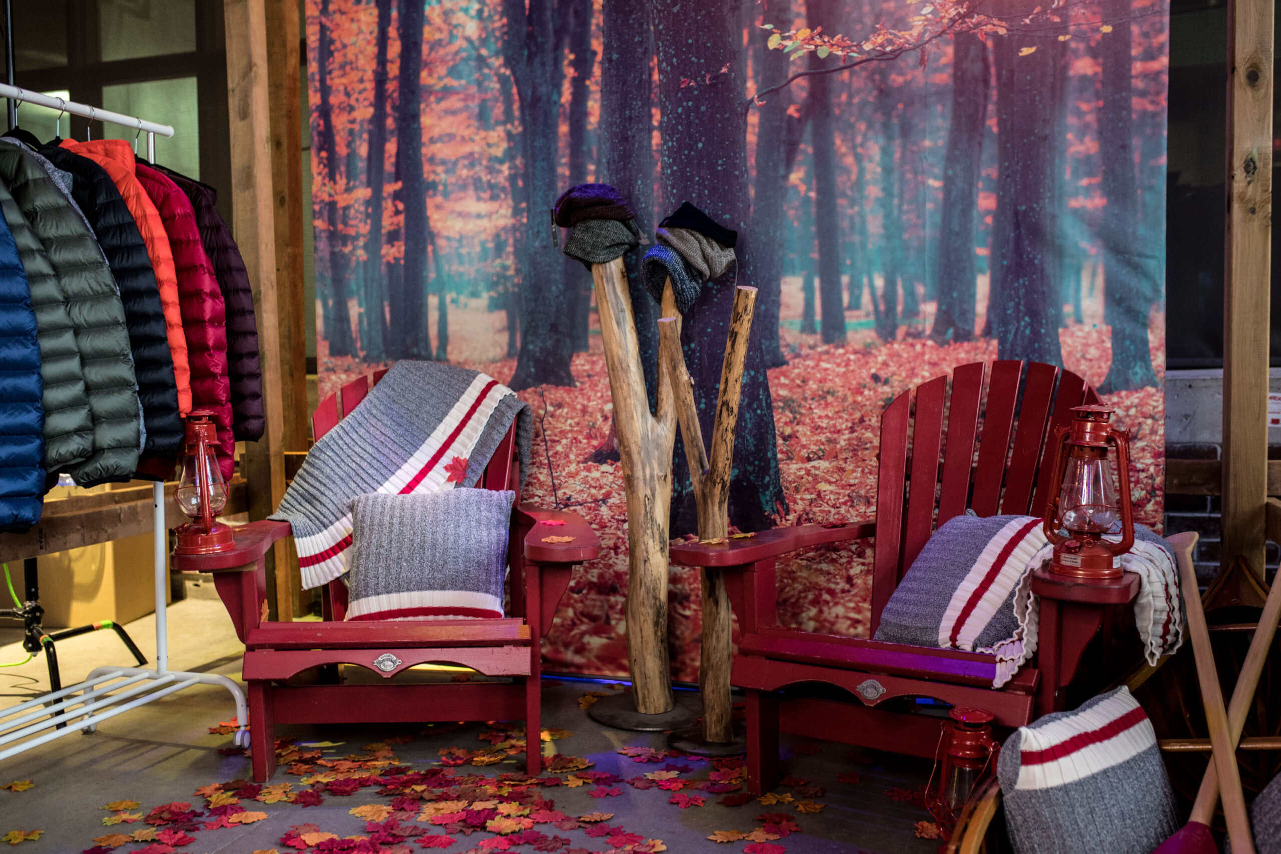 2 red Muskoka chairs with grey, red, and white blankets surrounded by fall leaves