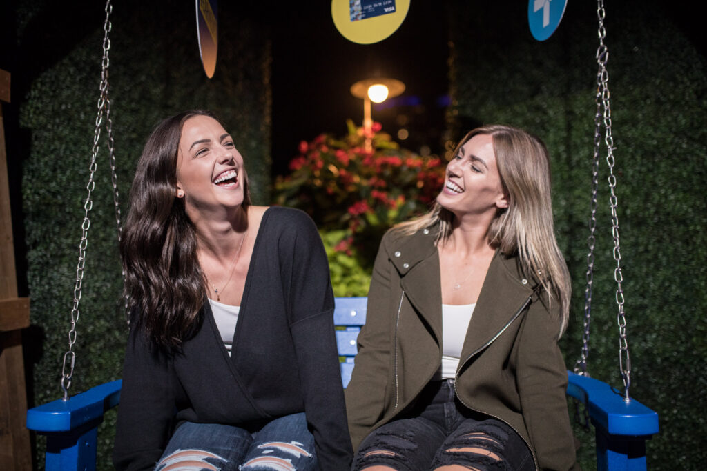 Two women smiling on a blue bench swing at the RBC Night On event