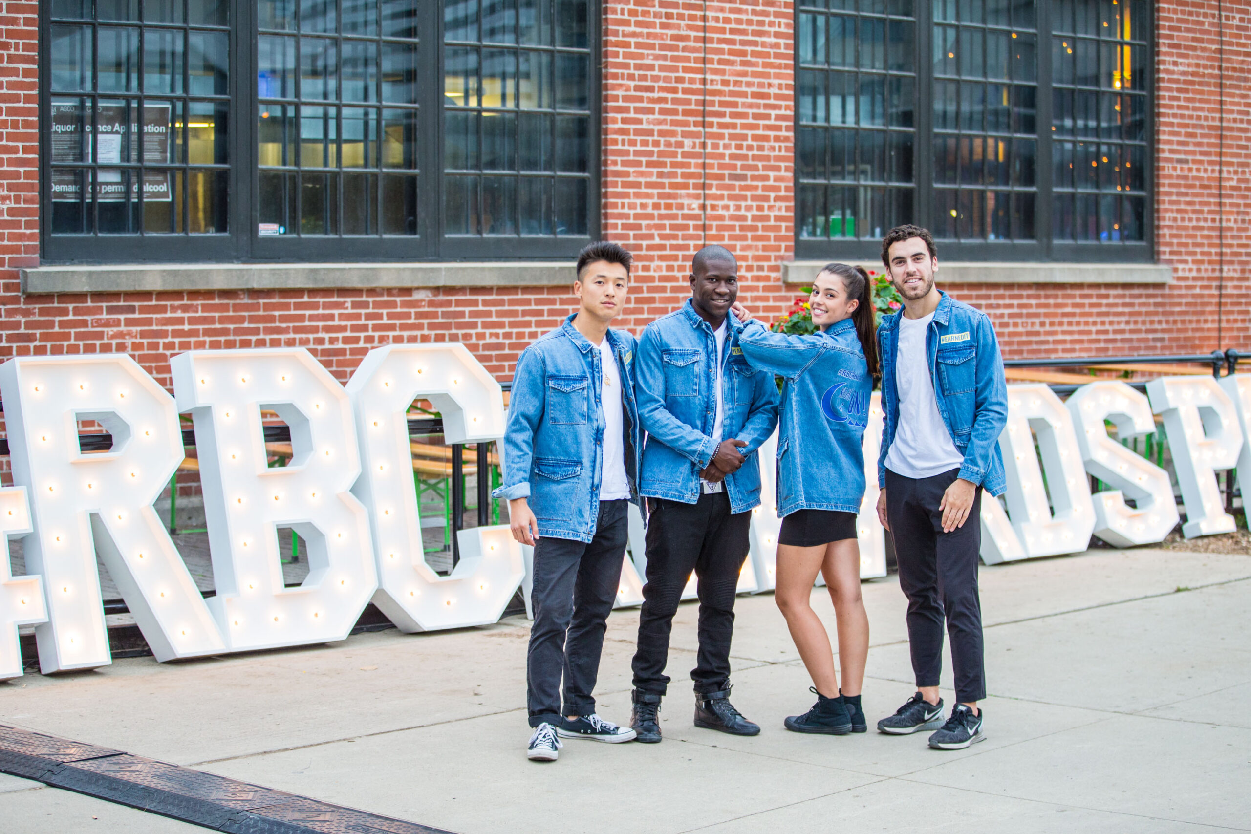 a group of young people posing in denim jackets in front of a brick building