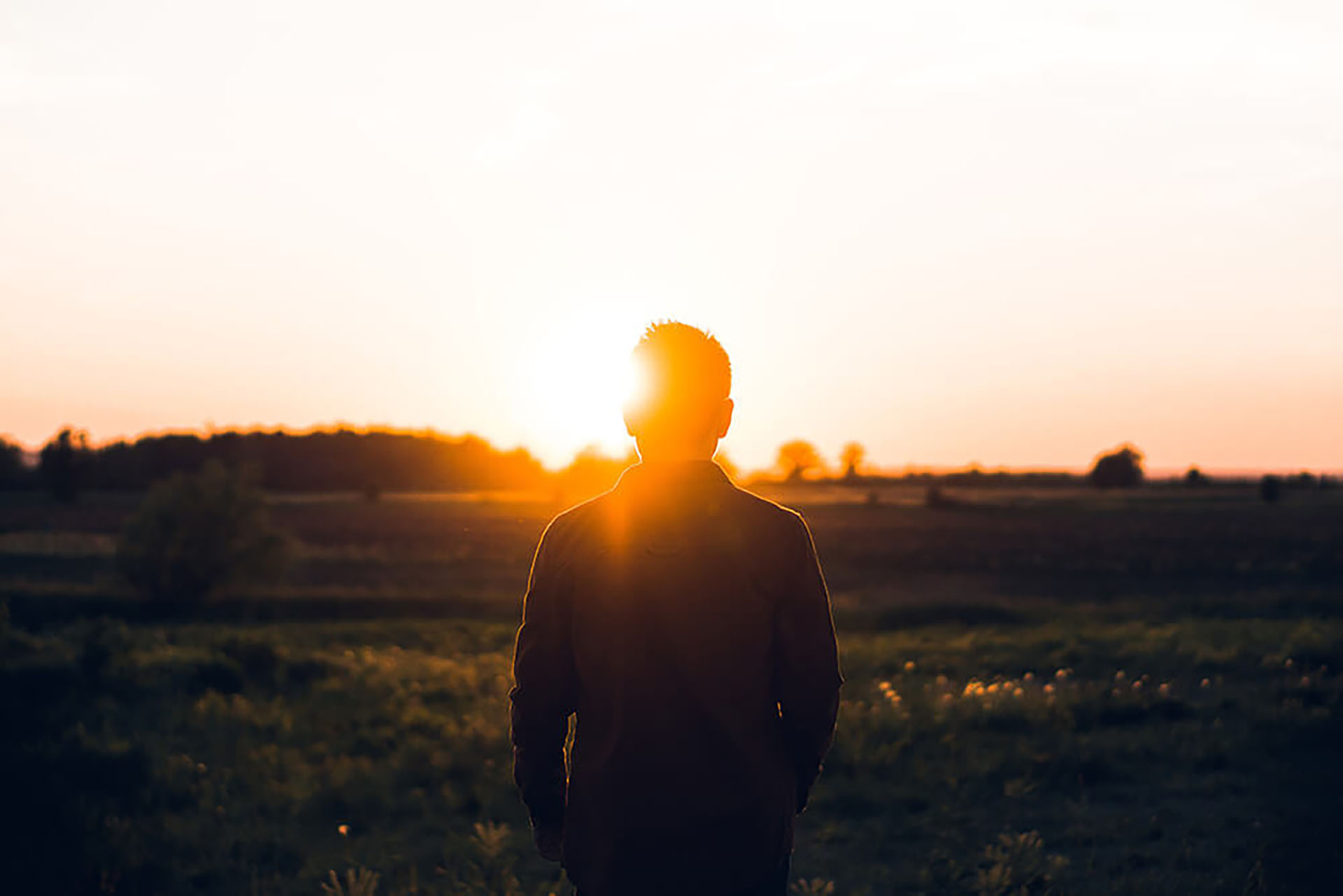 A man standing in a field looking at the sunset