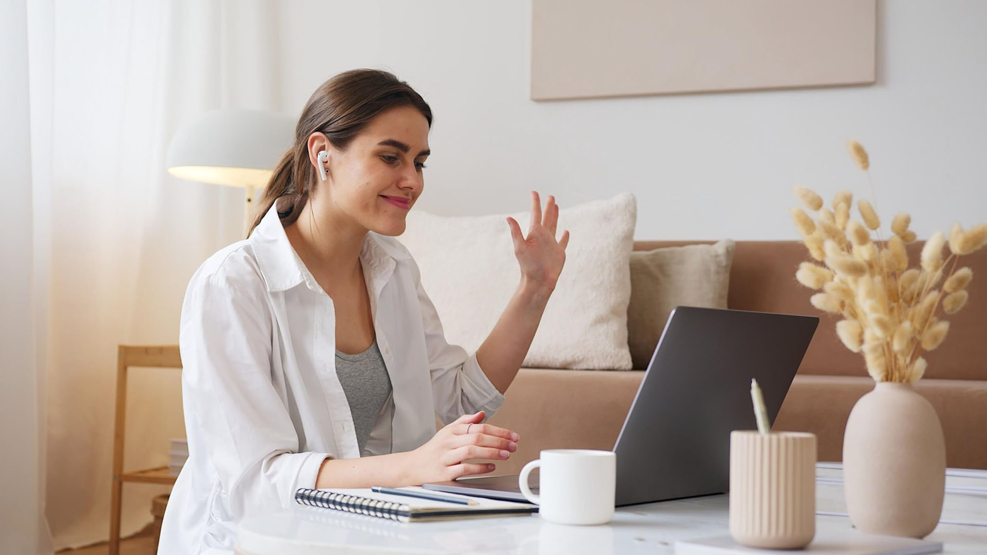 A woman waving at a laptop screen